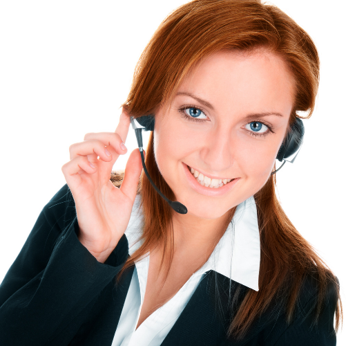 A person with long red hair is smiling and wearing a black blazer over a white shirt. They are holding the microphone part of a headset with one hand, perhaps indicating they manage outbound VoIP minutes as part of their role with a cloud Vicidial provider. The background is white.